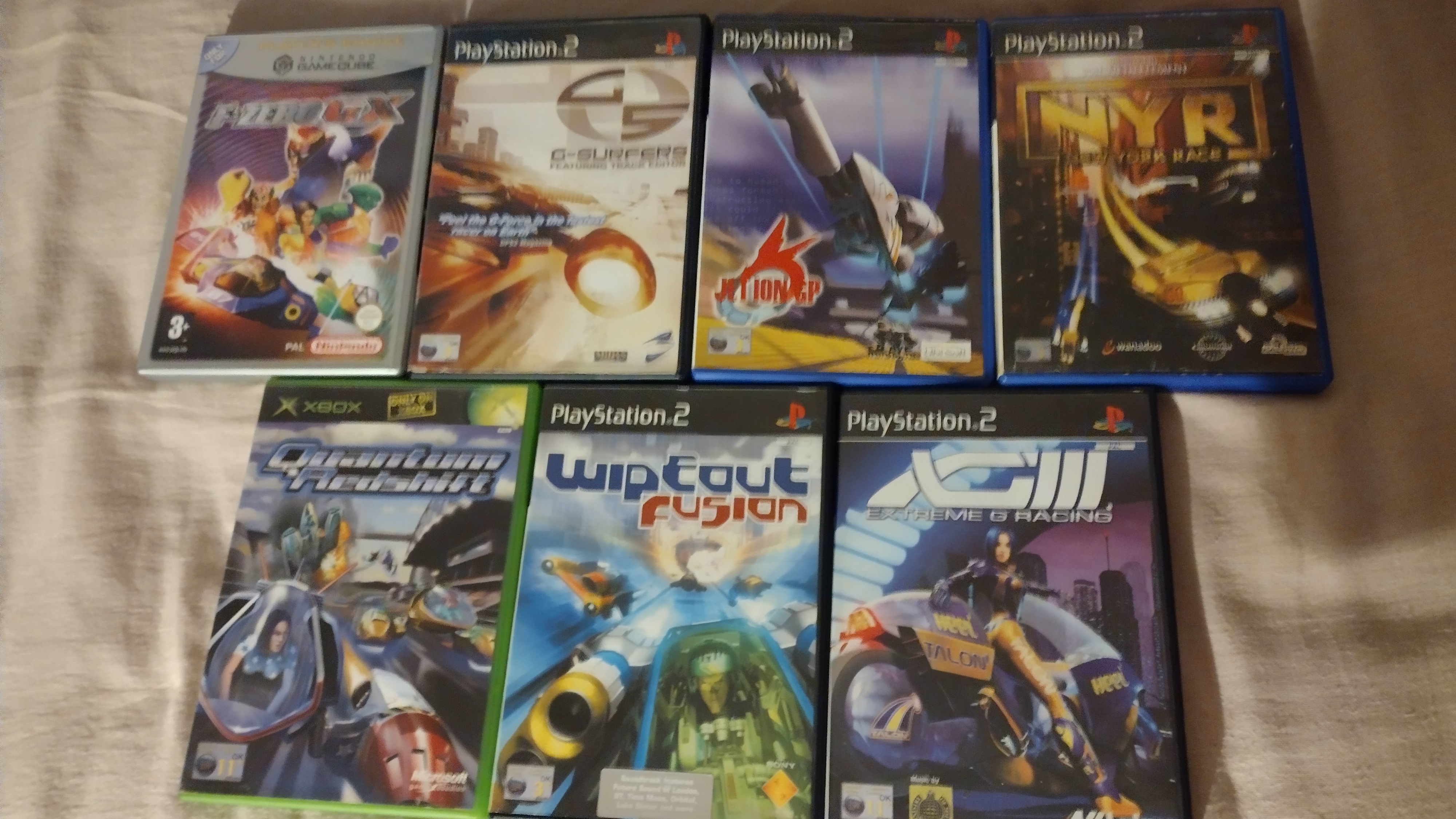 Keep cases for F-Zero GX, G-Surfers, Jet Ion GP, New York Race, Quantum Redshift, Wipeout Fusion, and Extreme G 3 laid out on a bedsheet.
